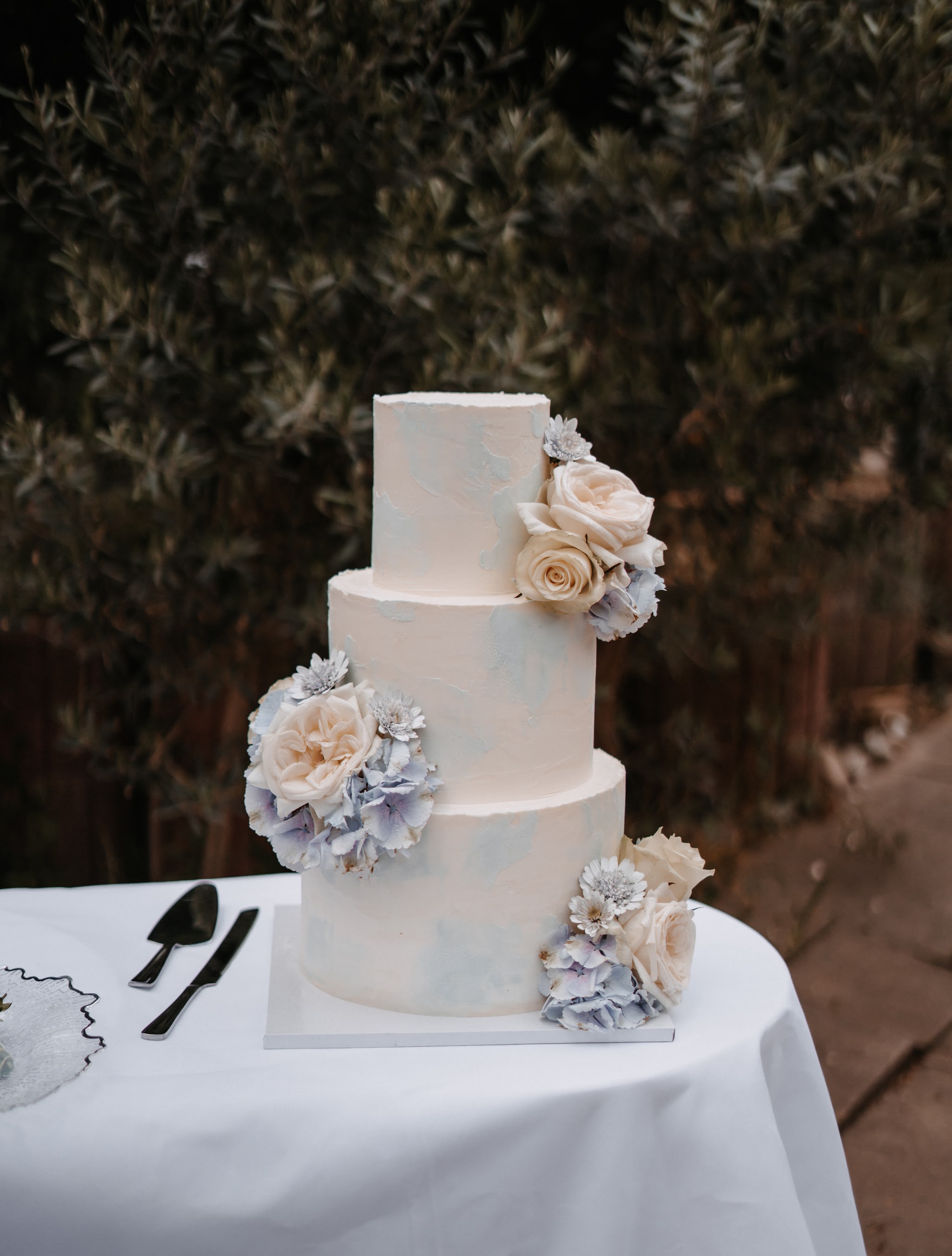 Dreistöckige Hochzeitstorte mit Rosen und Hortensien im Garten